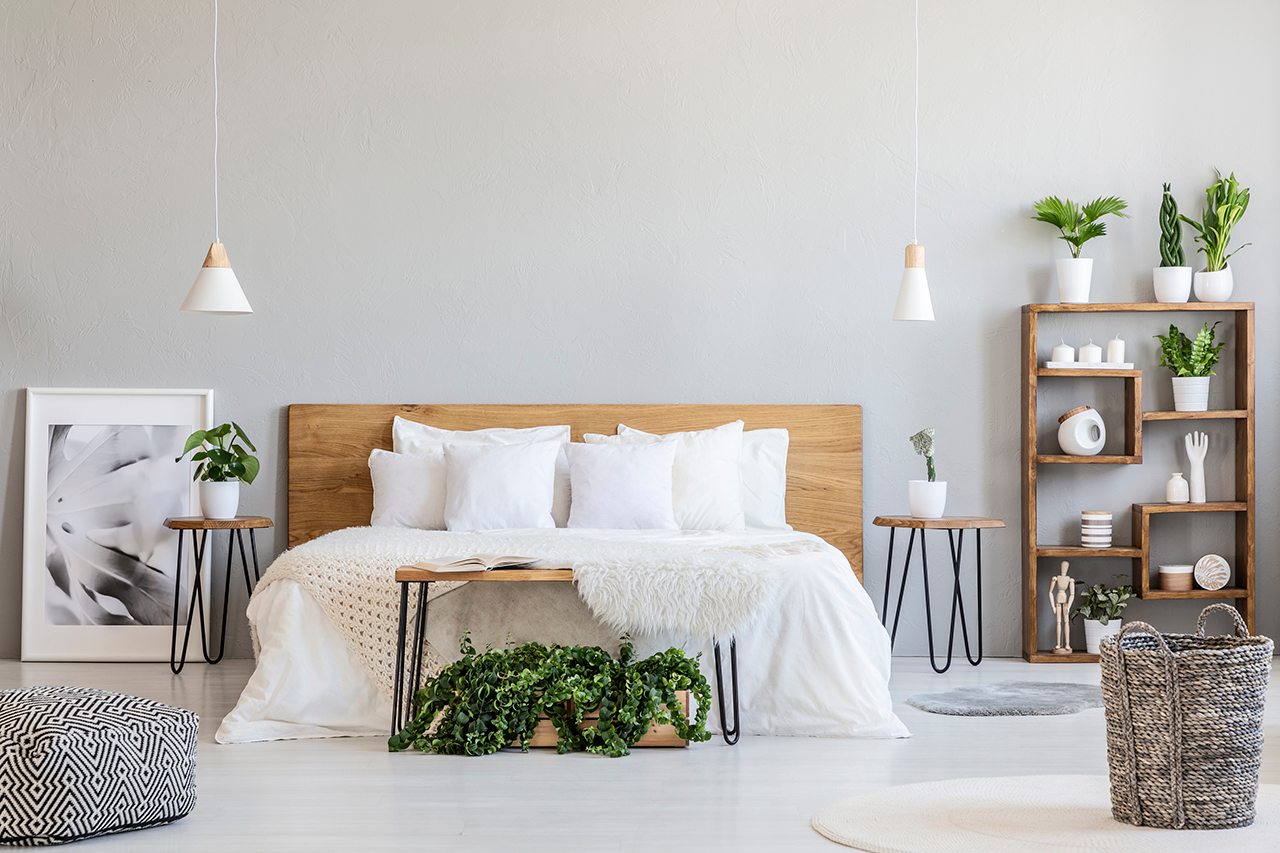 Patterned-pouf-and-basket-in-bright-bedroom-interior-with-lamps,-plants-and-poster-next-to-bed